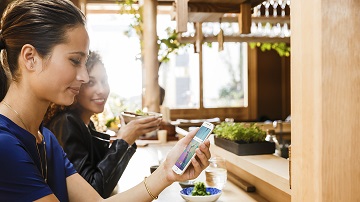 Two women looking at mobile phone while at lunch.